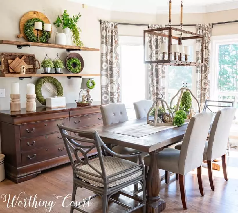 A dining room with a wooden table, a wooden hutch by the wall and a light fixture hanging above the wooden table.