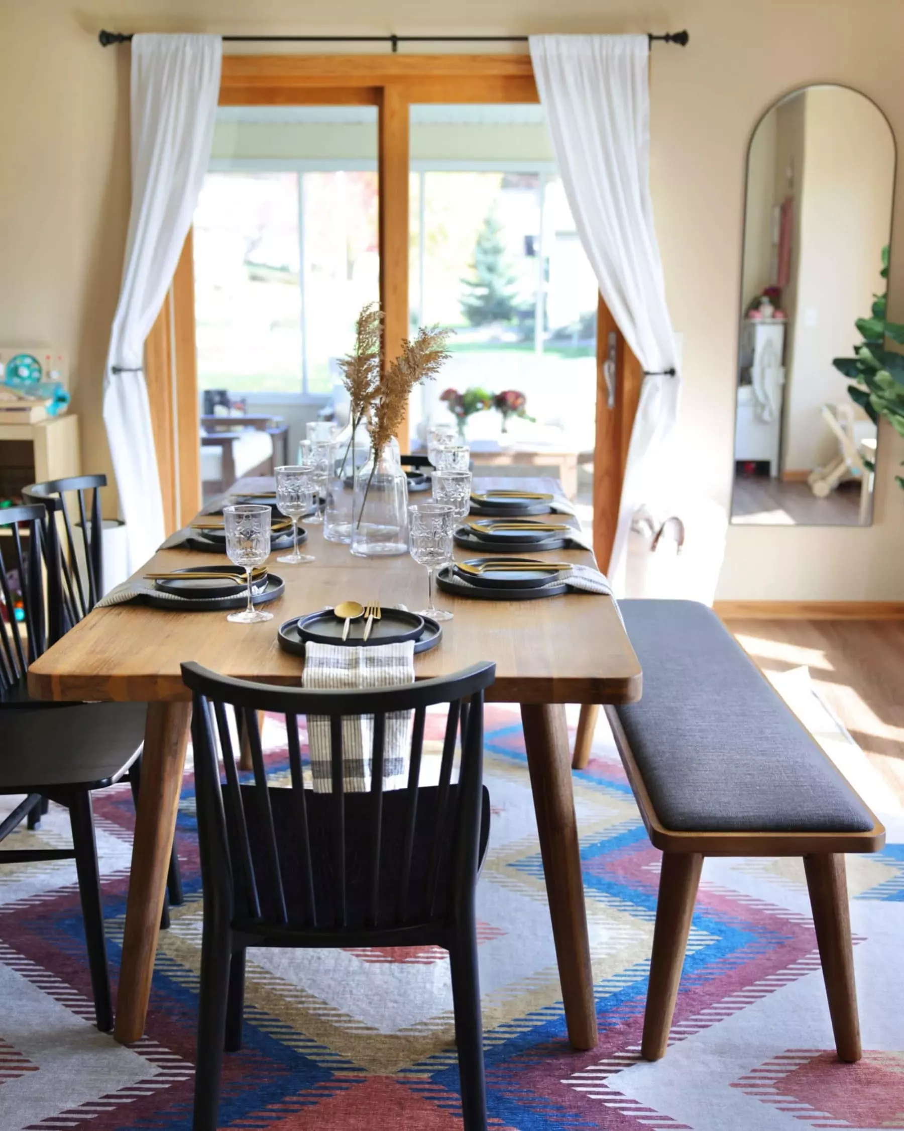 An extendable wooden dining table has plates, utensils, and glassware displayed on top.