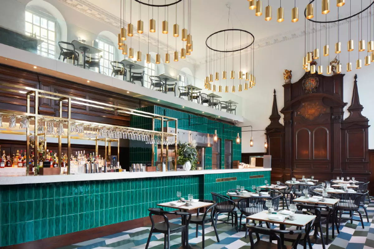 A green tiled bar stands out in this space with gold pendant lights from above.