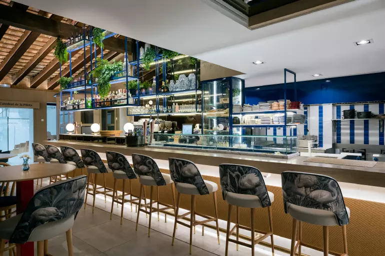 A wooden bar with green velvet bar stools features a canopy ceiling with metallic gold.