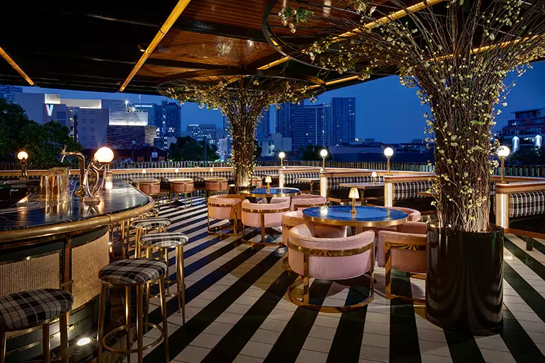 Greenery hangs from above at this bar that seems fit for a garden party with peach bar stools and blue chairs.