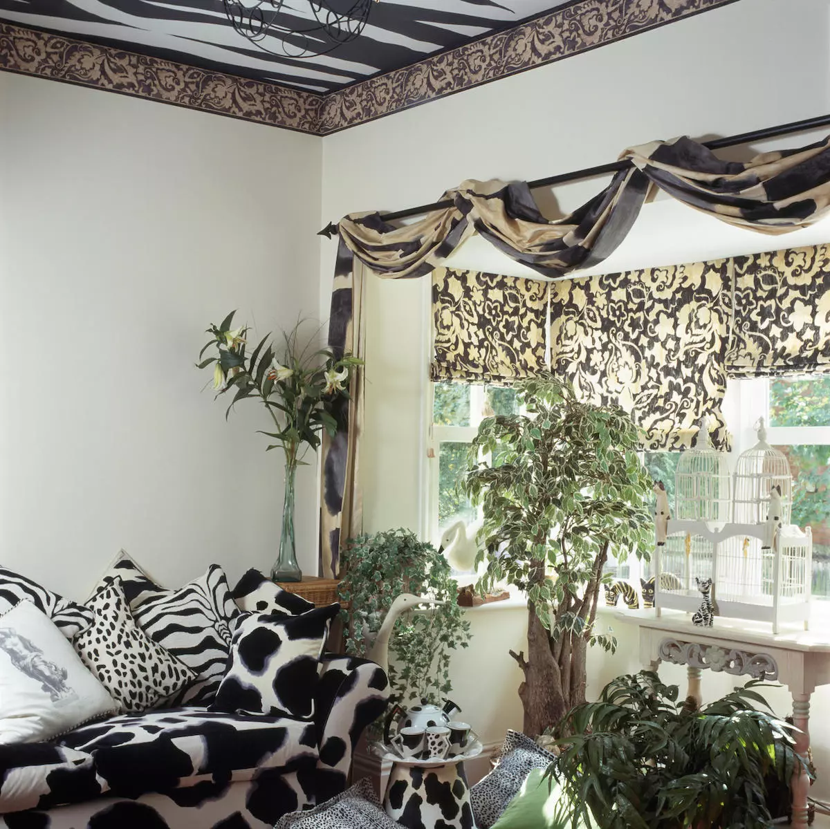 Black+white animal print sofa and cushions in nineties living room with draped fabric on pole above window