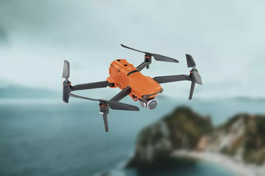 A black drone flying over a mountain and ocean.