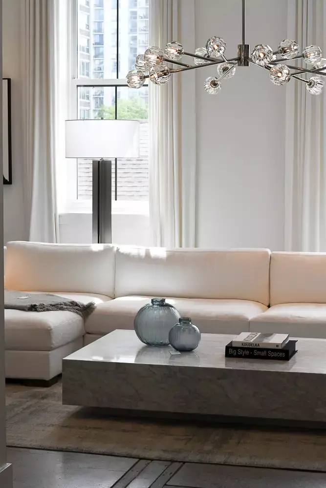 An L-shaped sofa in a neutral-colored room with sheer curtains flanking the large rectangular window behind it