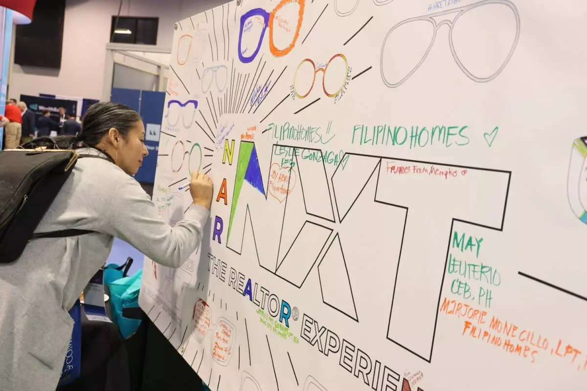 A woman helps color a sign that says NXT the realtor experience on the expo floor of NAR NXT 2023