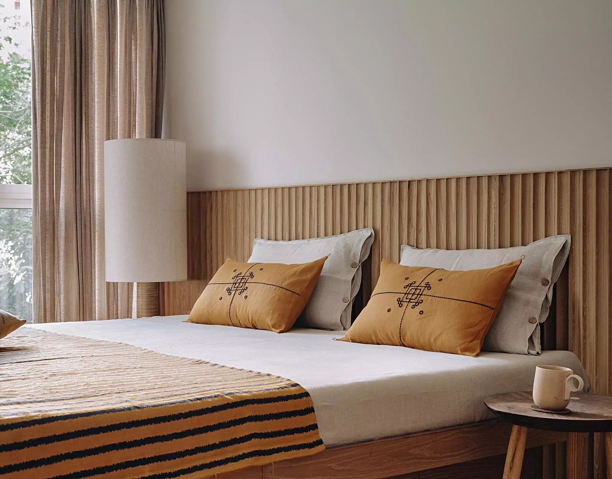 Japandi bedroom with orange throw pillows, fluted wood wall panelling, and warmly colored bedding