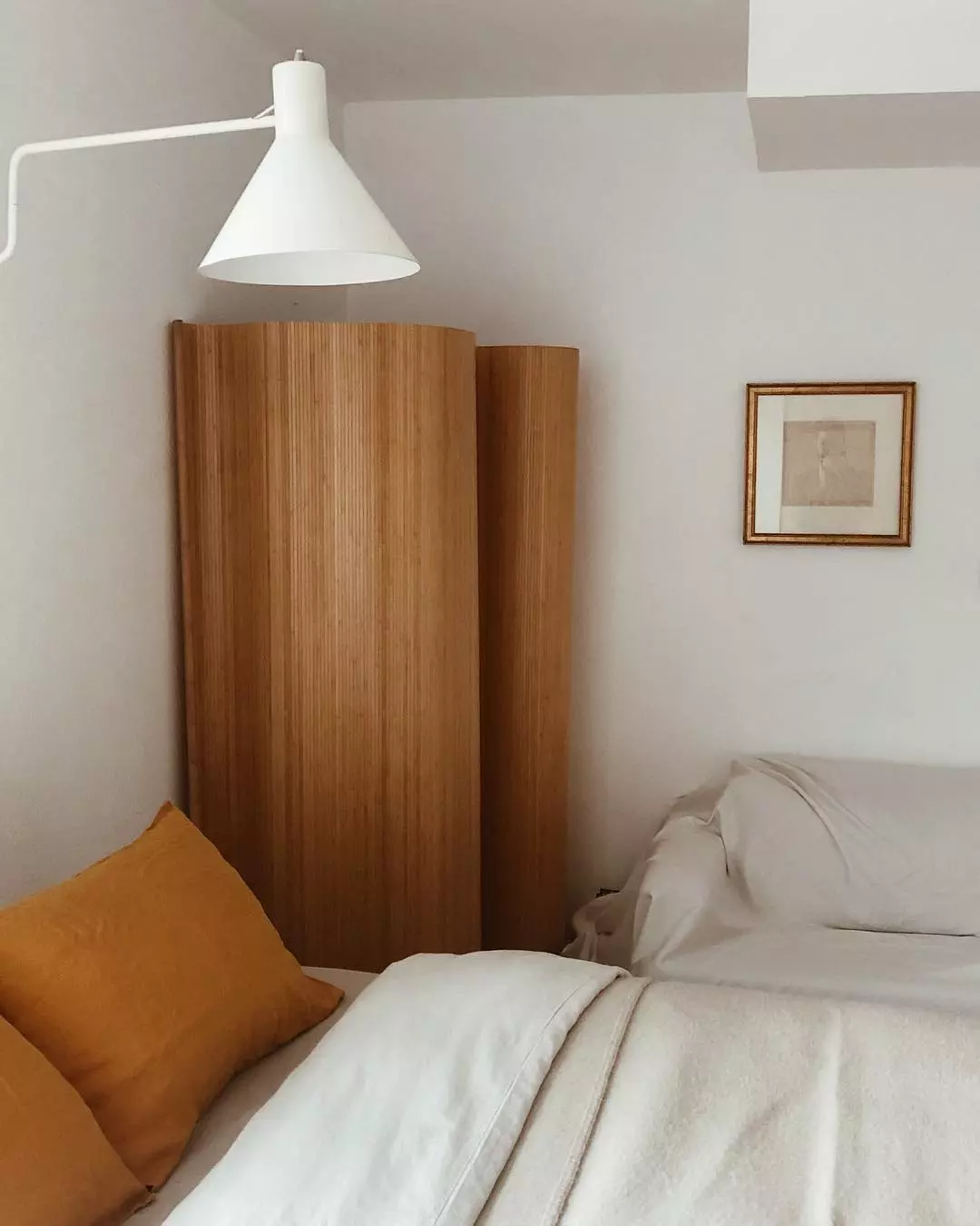 Minimalist Japandi bedroom with a flexible wood slat room divider and framed vintage wall art