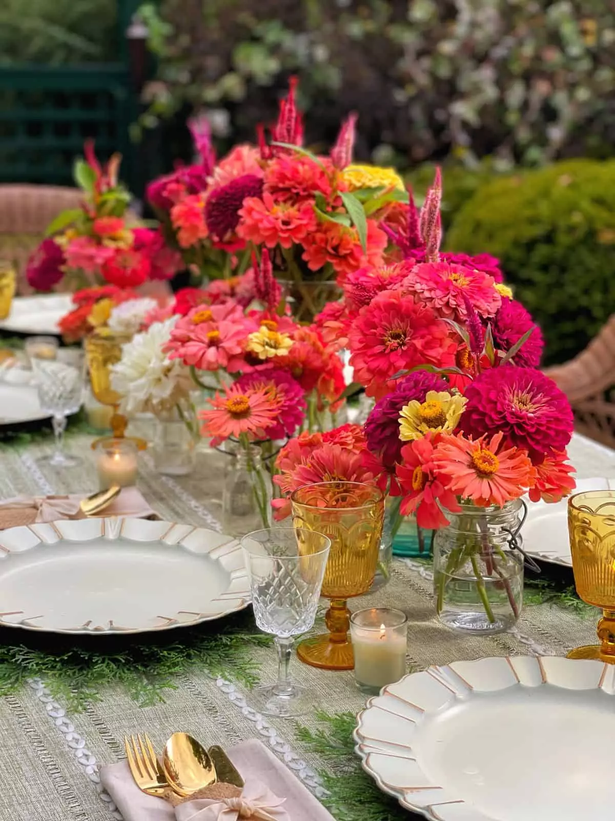 Close up of the fresh-cut zinnias and celosia in glass vases and vintage mason jars on a farmhouse table set for a garden party