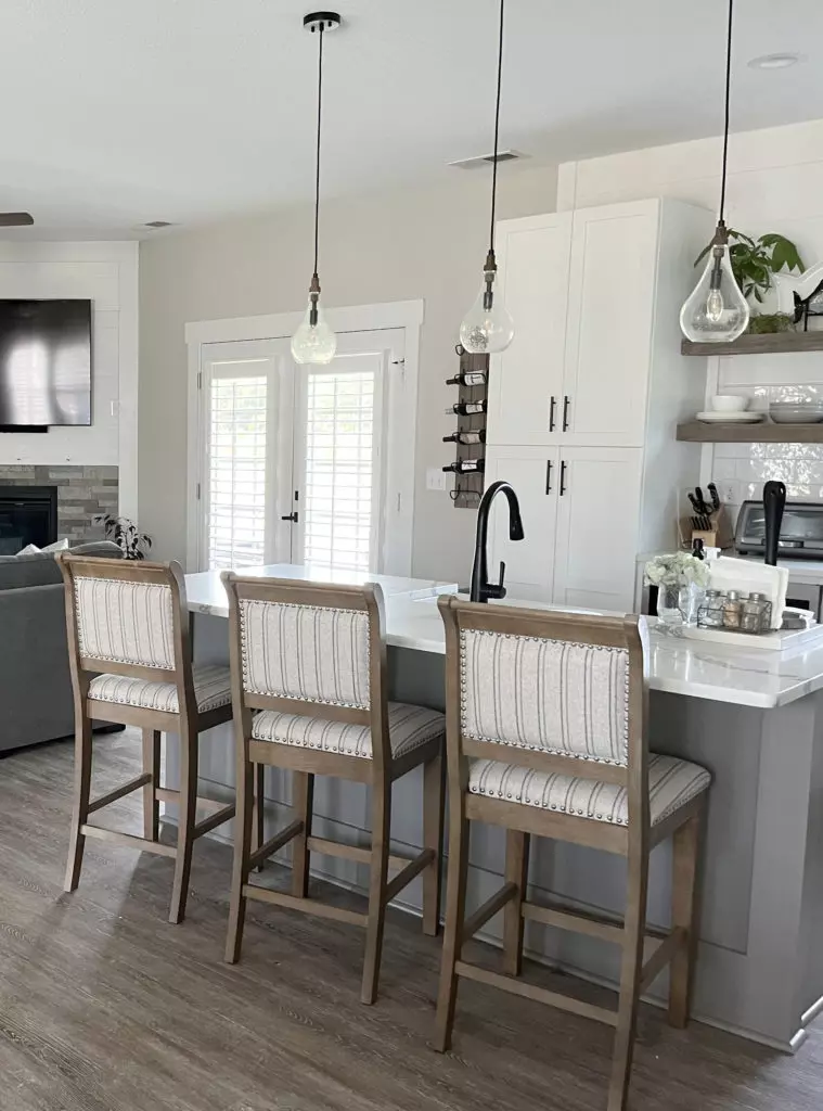 Sherwin Williams Agreeable Gray best greige warm gray paint color, wood laminate gray wash floor, corner fireplace, white kitchen cabinets, Dovetail island.