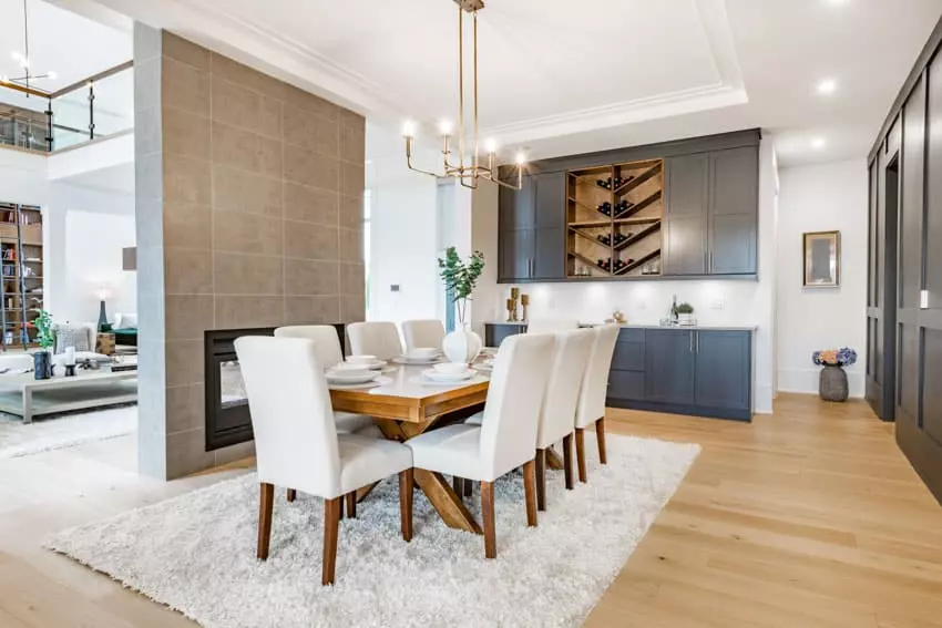 Transitional dining room with table, white chairs, chandelier, bar counter, rug, and wood flooring