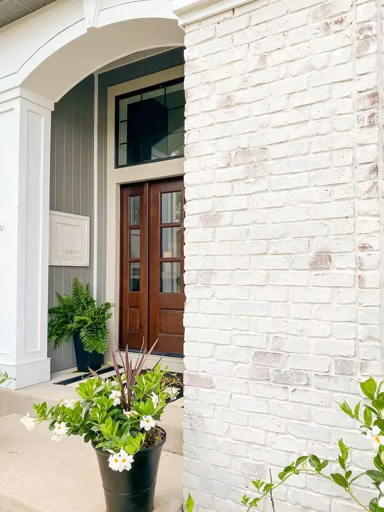 Limewashed brick and a view of a front porch with a dark-colored wooden door