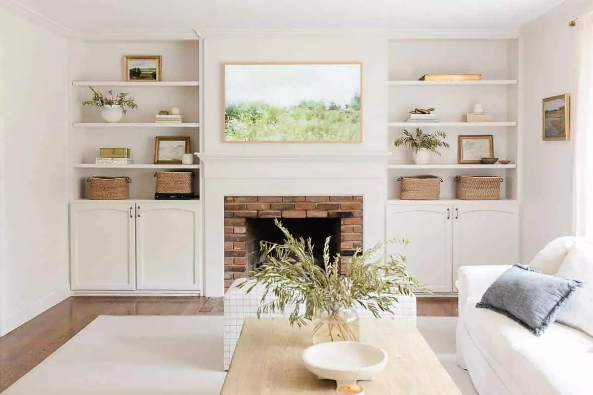 A white living room with bookshelf decor.a brick fireplace surrounded by built-ins.