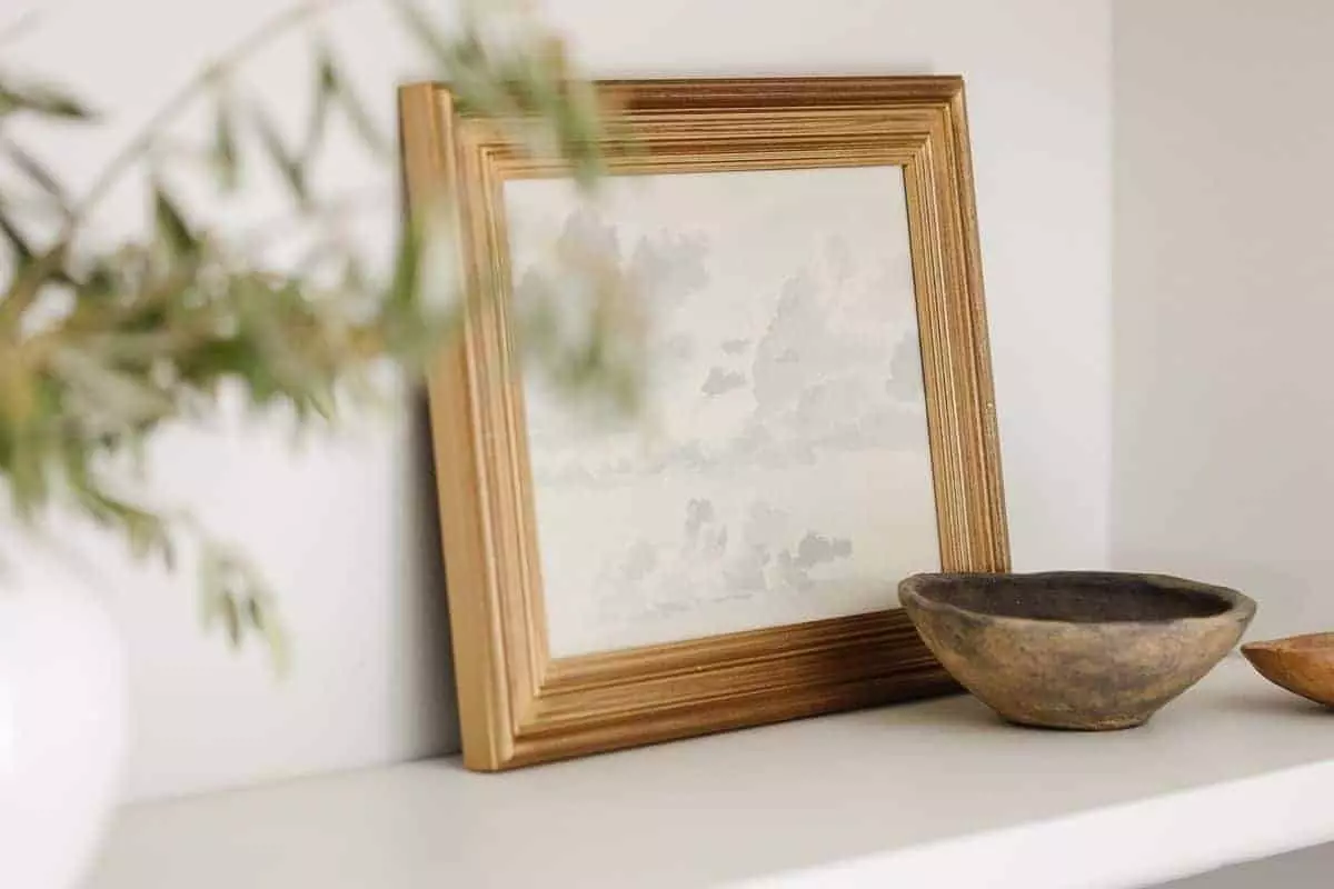 A white pottery vase full of greenery with books and bookshelf decor above.