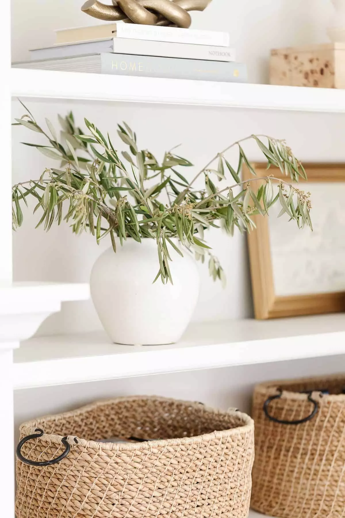 Bookshelf decor ideas of baskets, white pottery, and artwork on white built-ins.