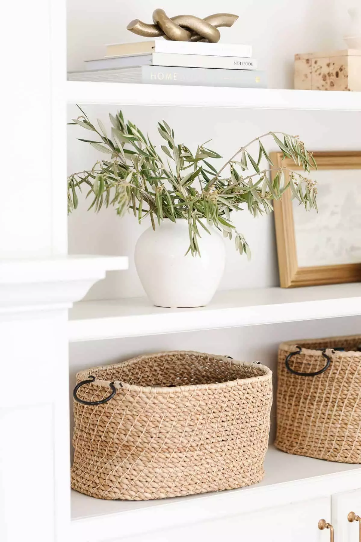 Bookshelf decor ideas of baskets, white pottery, and artwork on white built-ins.