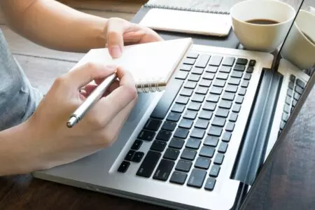 Woman writing investment trust income research notes and using a laptop