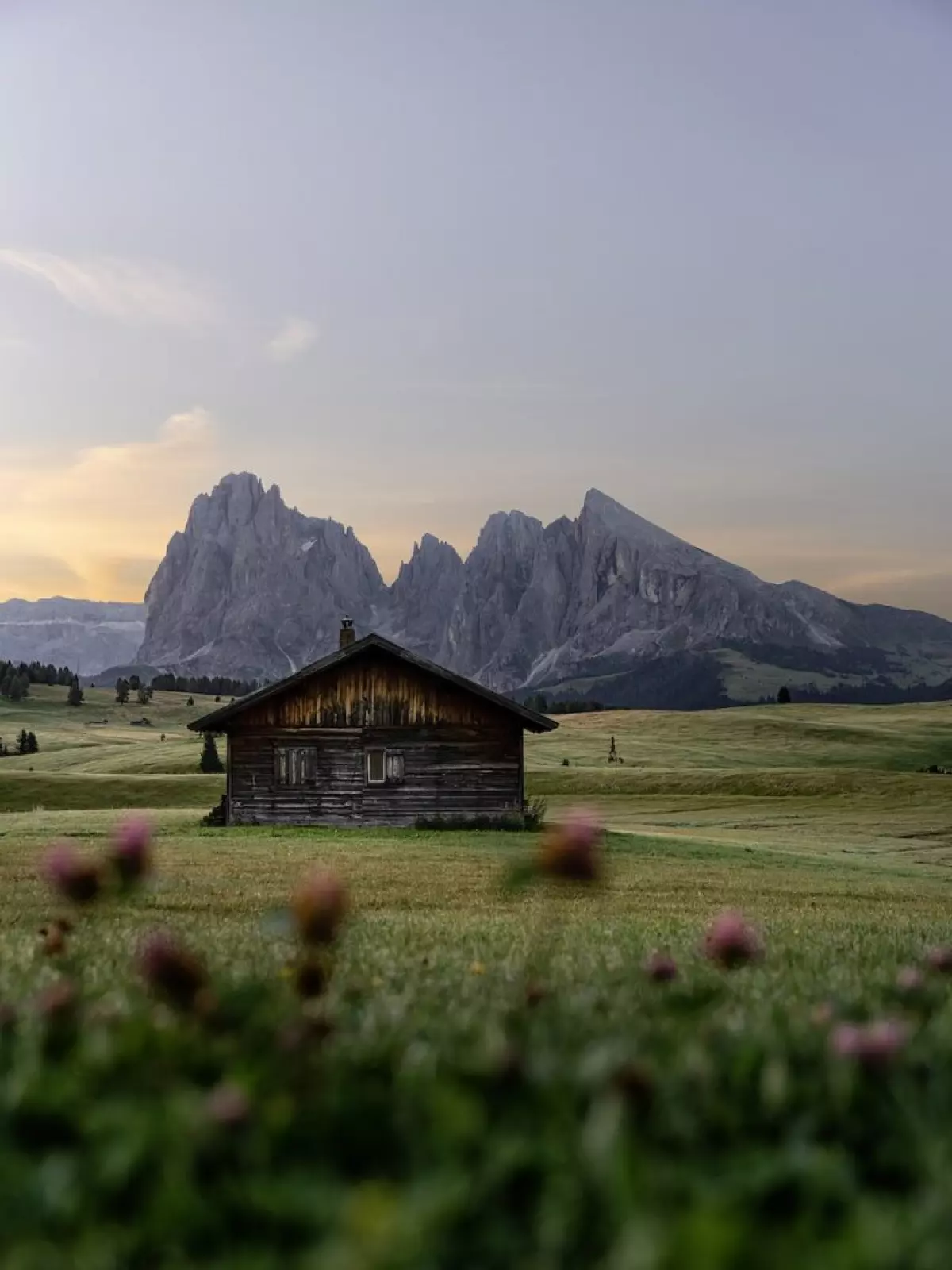 Picturesque view of aged wooden house on green lawn behind rough rocks under cloudy sky at sunset