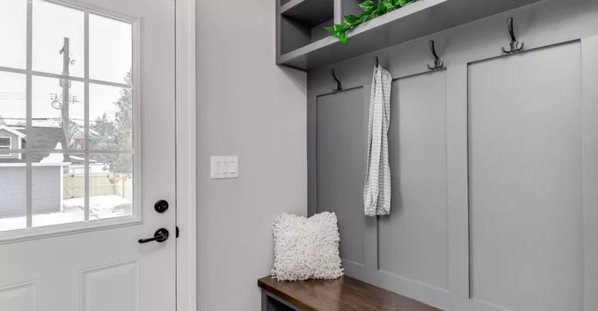 A staged, gray mudroom / entryway with bench seating, coat hooks