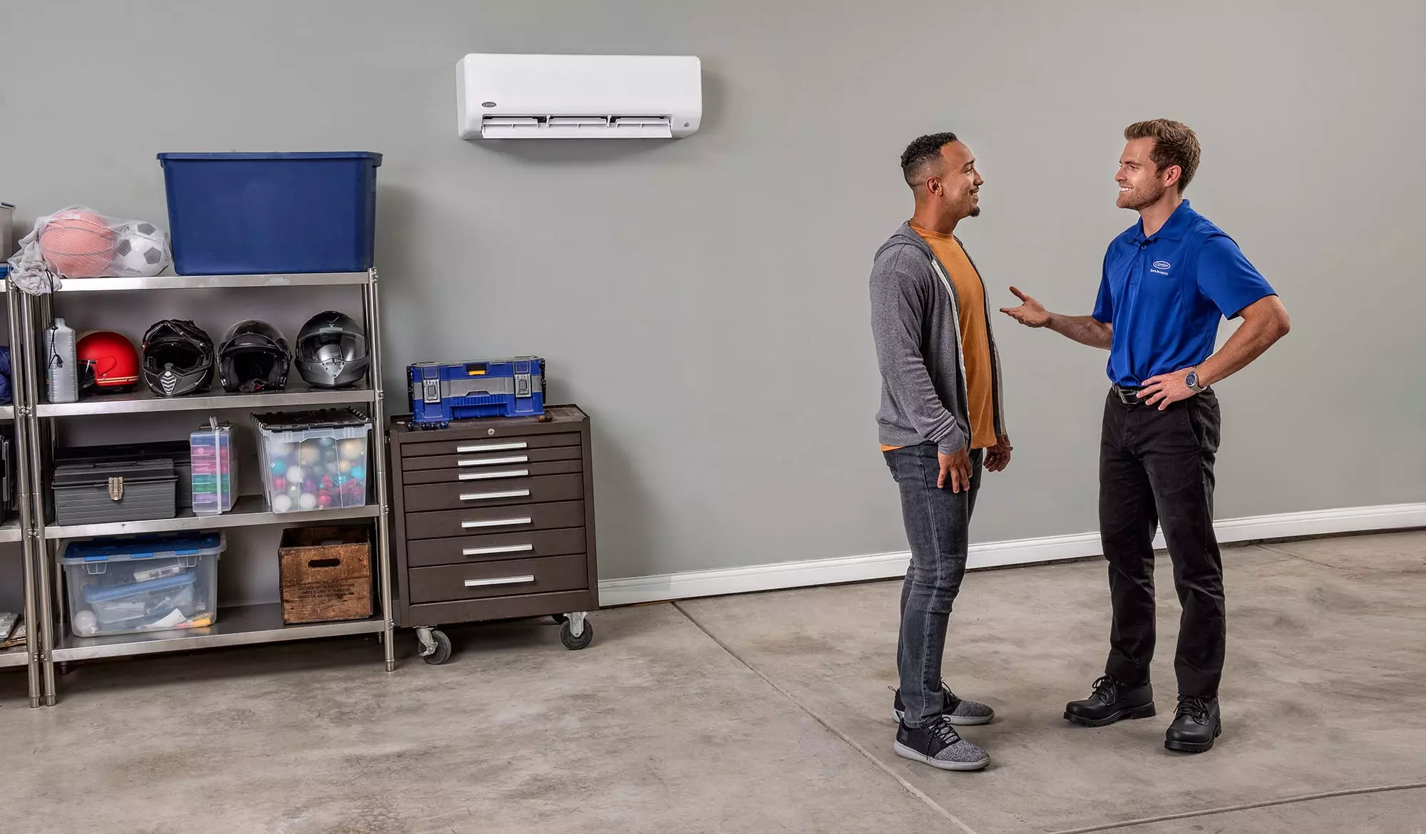 A Carrier dealer in a garage talking to a man after mini split installation.