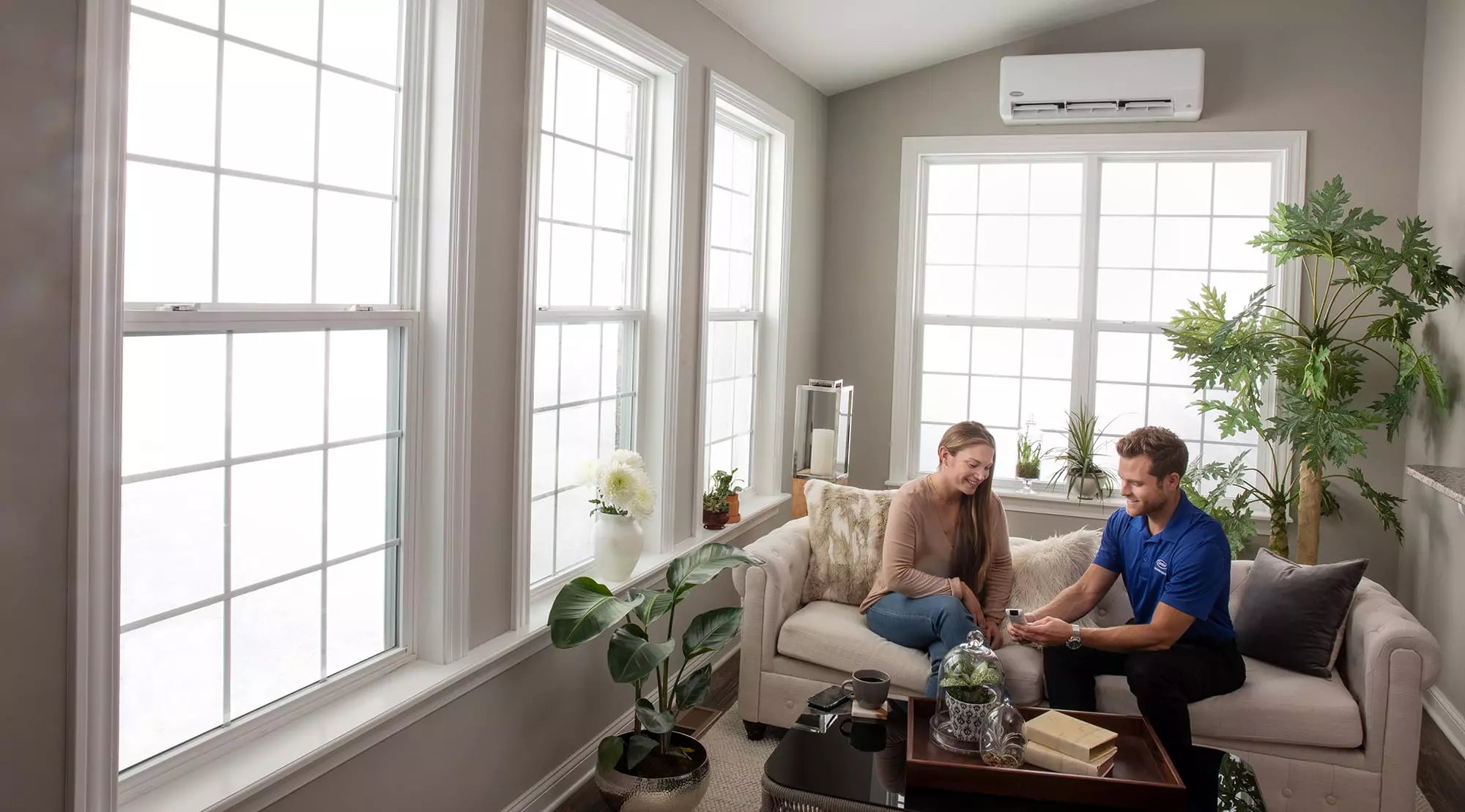 A Carrier expert on a couch explaining ductless air conditioner installation to a woman.