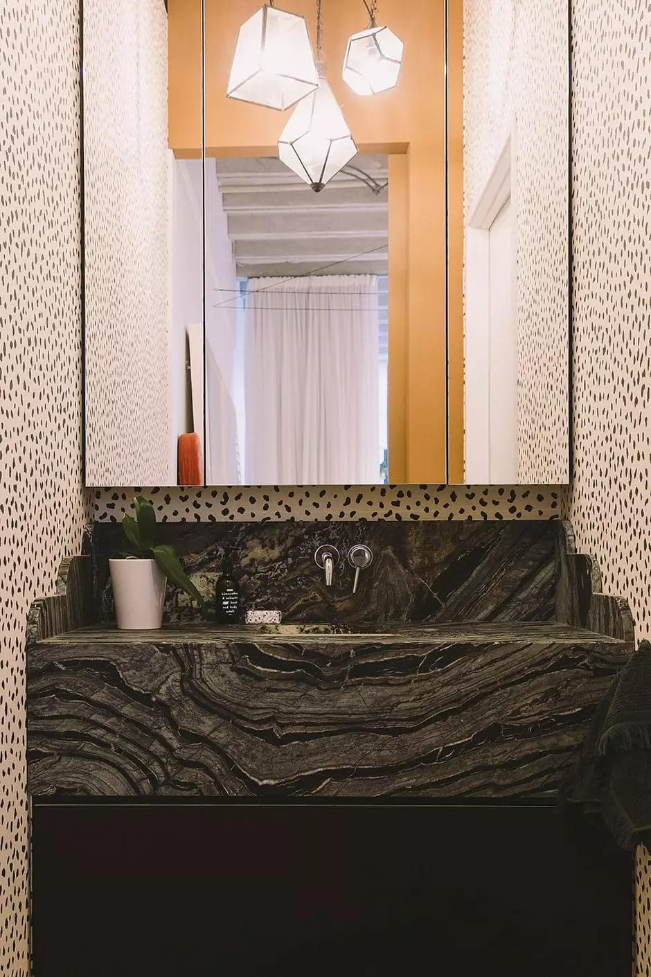 ABOVE Janice designed this shaped vanity then had it made in Silver Brown Wave marble by Italian Stone. The mirrored cabinetry and wall-to-wall drawers are another Mr & Mrs Ward creation. Wallpaper by Thibaut surrounds it all, lit by pendant lights picked up in Bali.