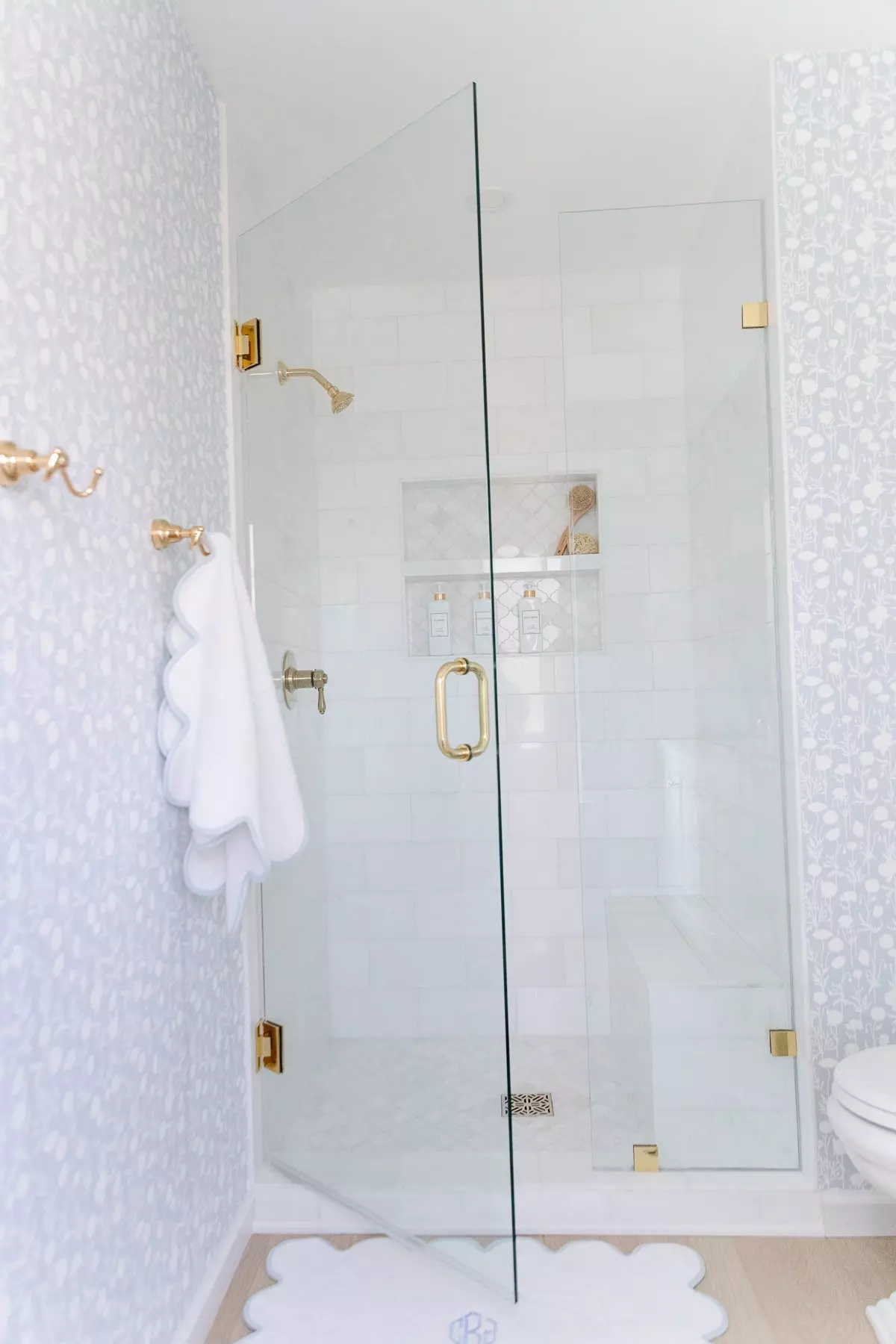 A white and gold bathroom featuring serena and lily wallpaper and a glass shower door.