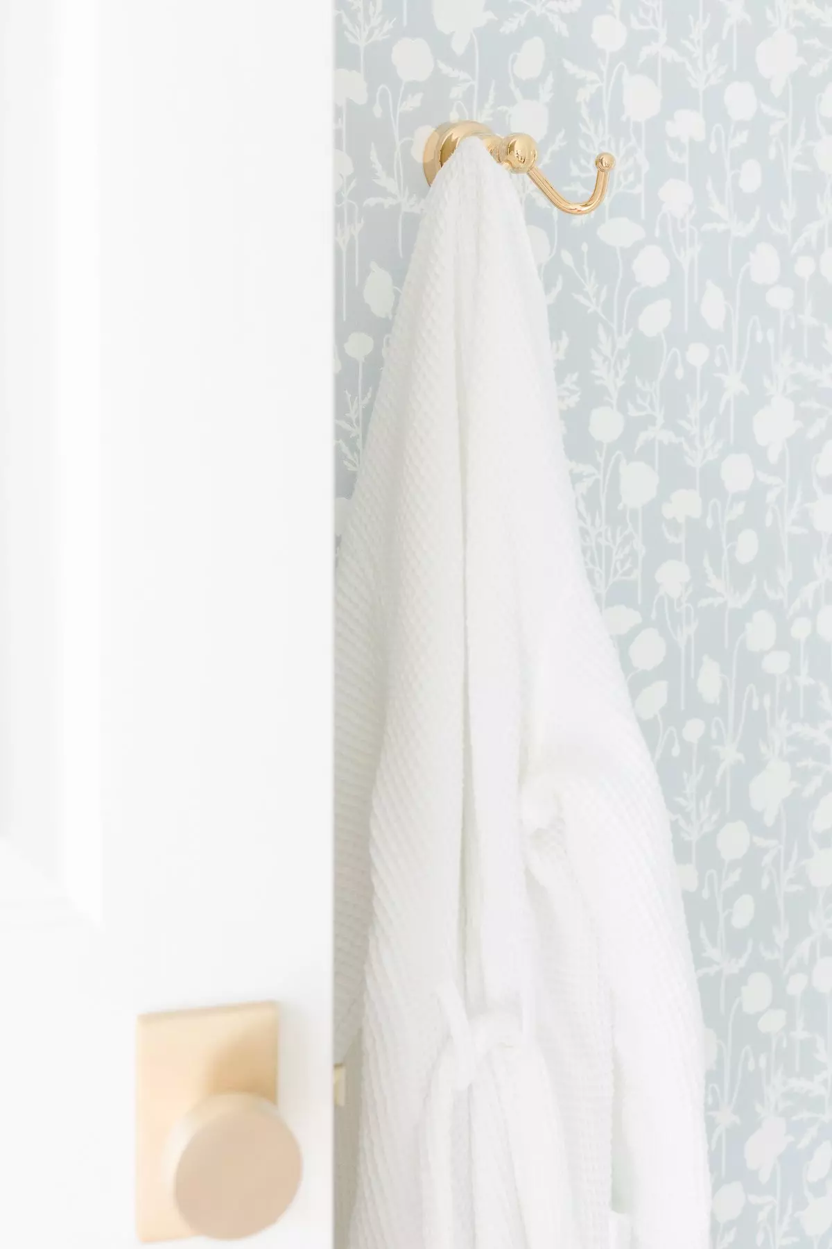 A white towel hangs on a hook in a bathroom featuring Serena and Lily wallpaper.