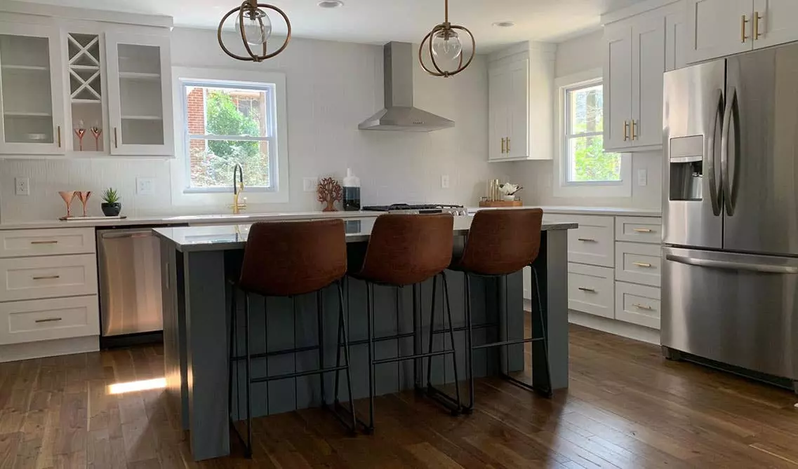 White cabinets kitchen with black accents, pendant lights, large island with sink, and metal chair