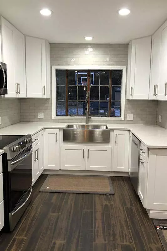 L-shaped kitchen design with white cabinets, large island with stacking chairs, pendant lights, and SPC flooring