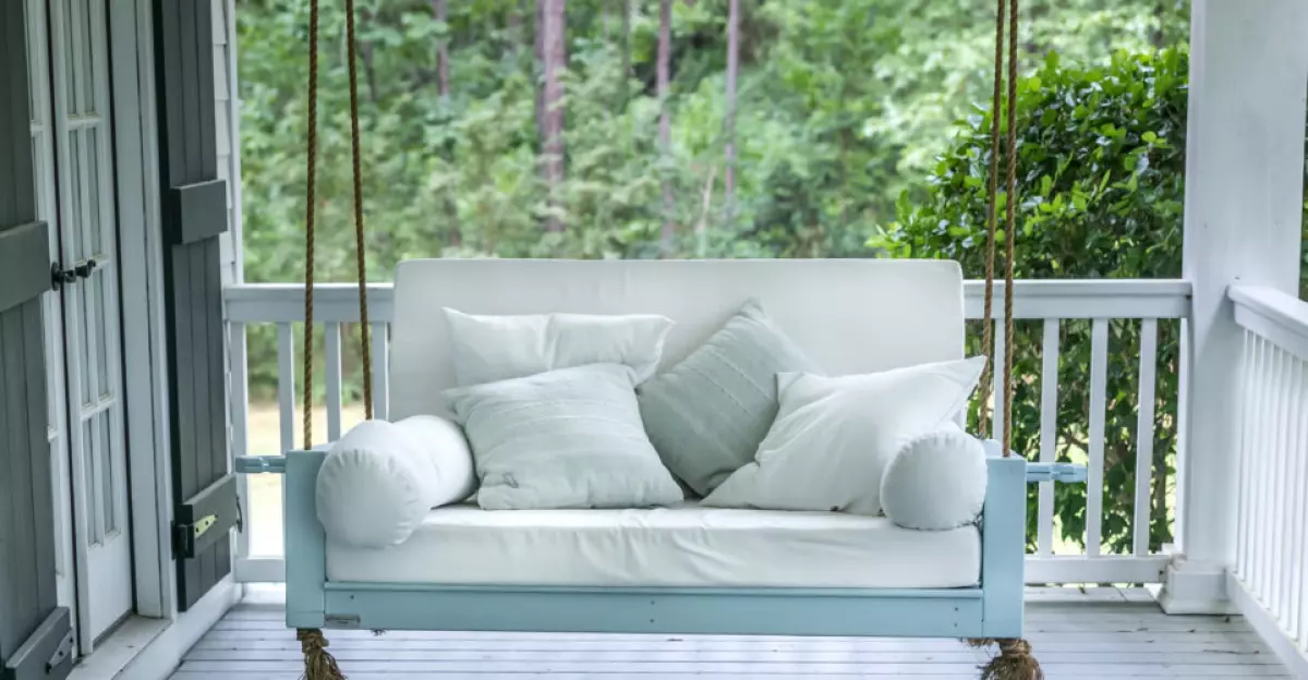 A luxurious and classic outdoor bed swing painted a seafoam green with white deep cushions and the swing is hung from the ceiling by rope.