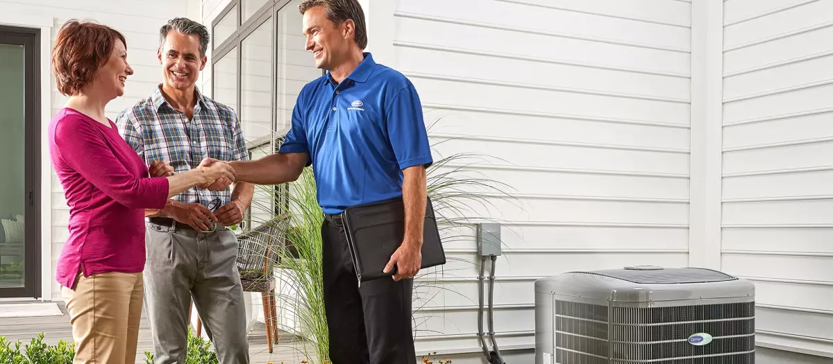 A couple shaking hands with dealer next to ac after air conditioner maintenance