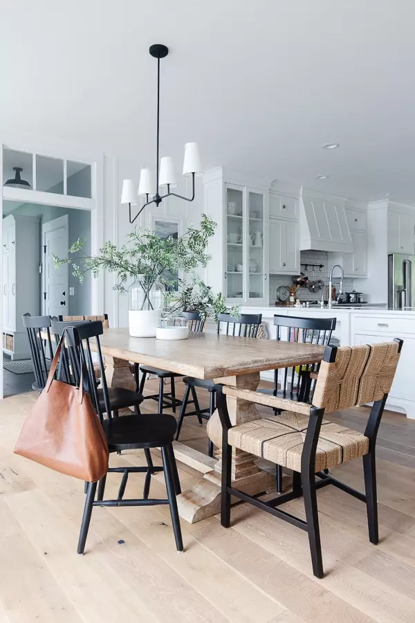 white lake house dining room with wood table and black and woven chairs adjacent to white kitchen