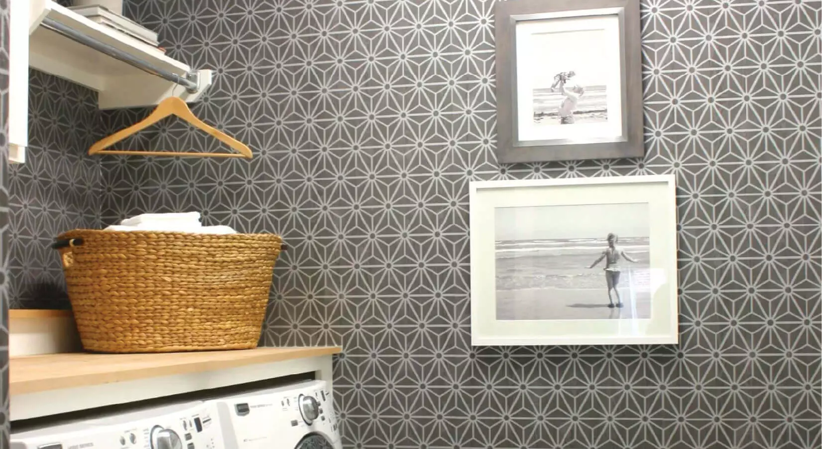 Laundry room with folding table on top of appliances, gray patterned wallpaper, and family photos.