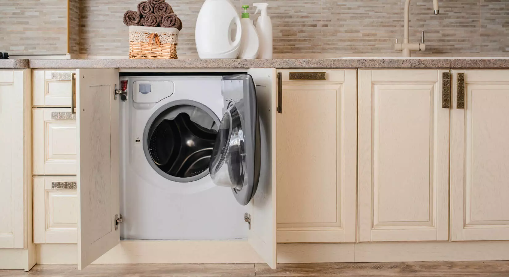 Washer hidden in cream cabinets underneath a kitchen sink.