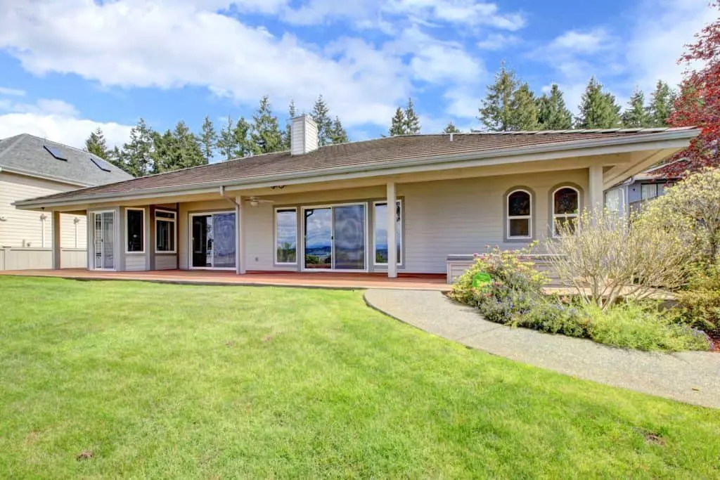 A contemporary ranch-style house with beige painted sidings, shingle roofing, and a freshly mowed lawn