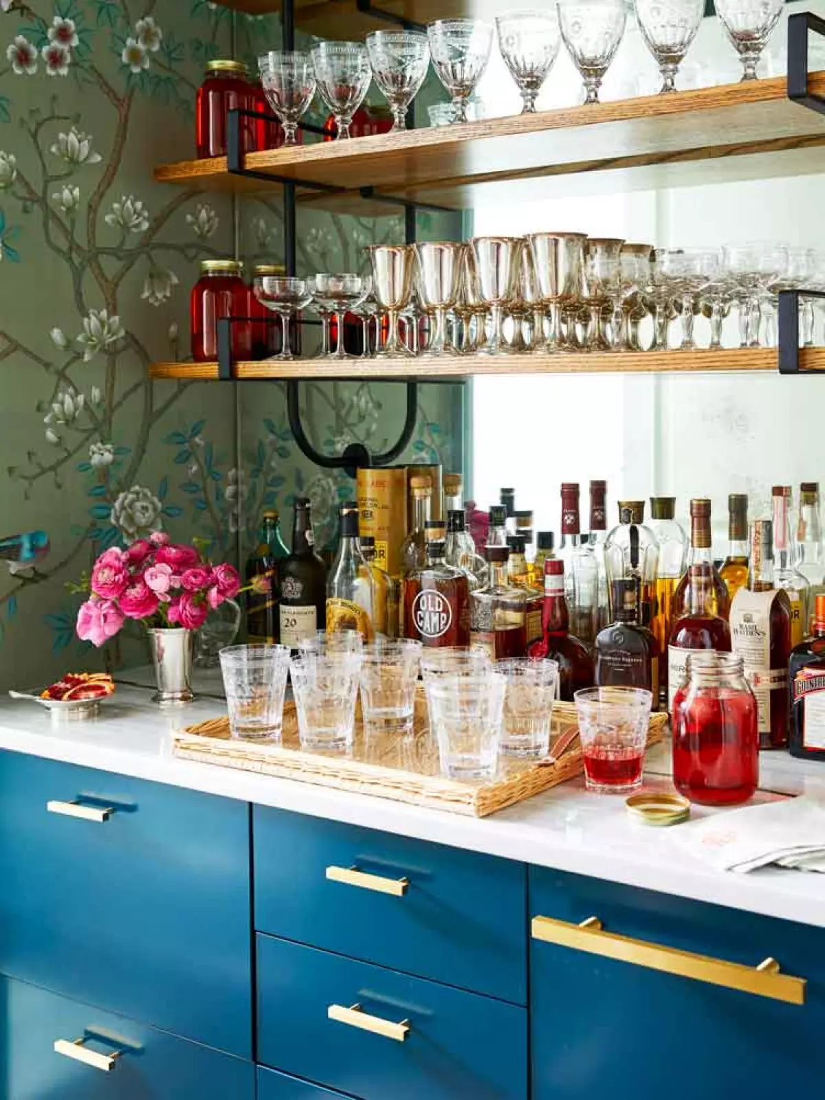 Bar area with floral, emerald wallpaper houses an array of delicate cocktail glasses.