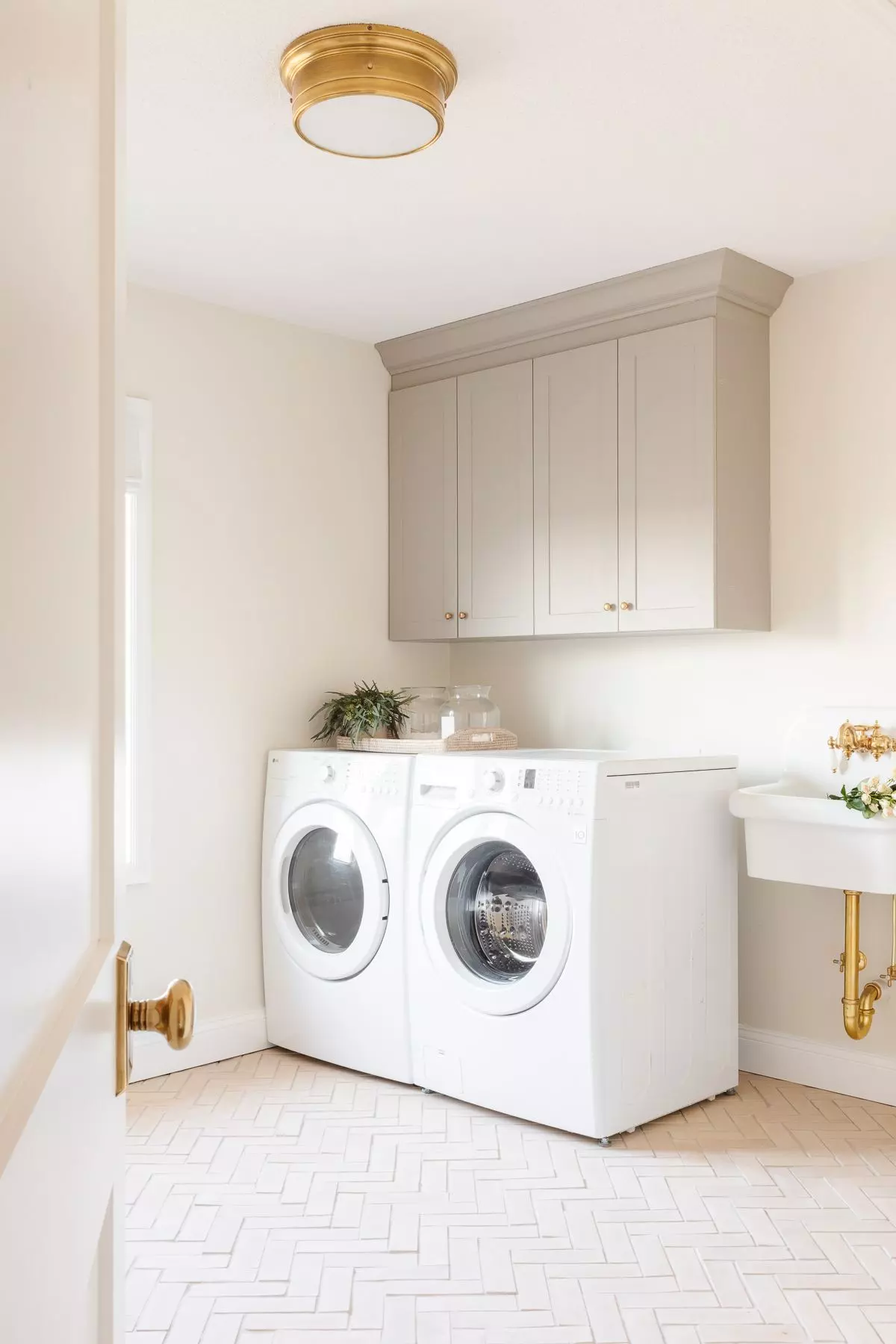 A laundry room with cream walls, greige cabinets and herringbone floors.