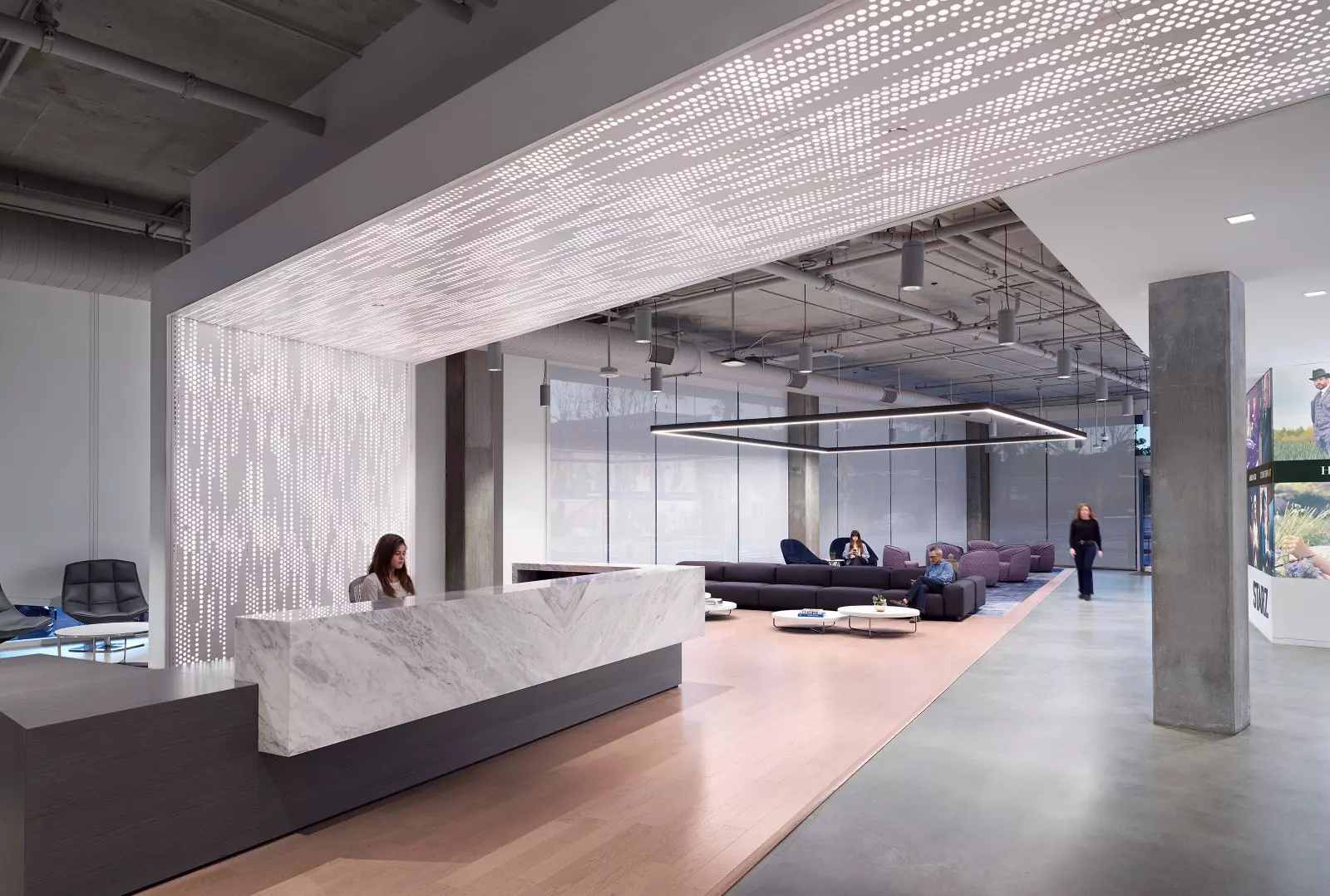 This lobby space has a marble front desk with a person sitting behind it. There is a seating area with gray sofas towards the back of the space.