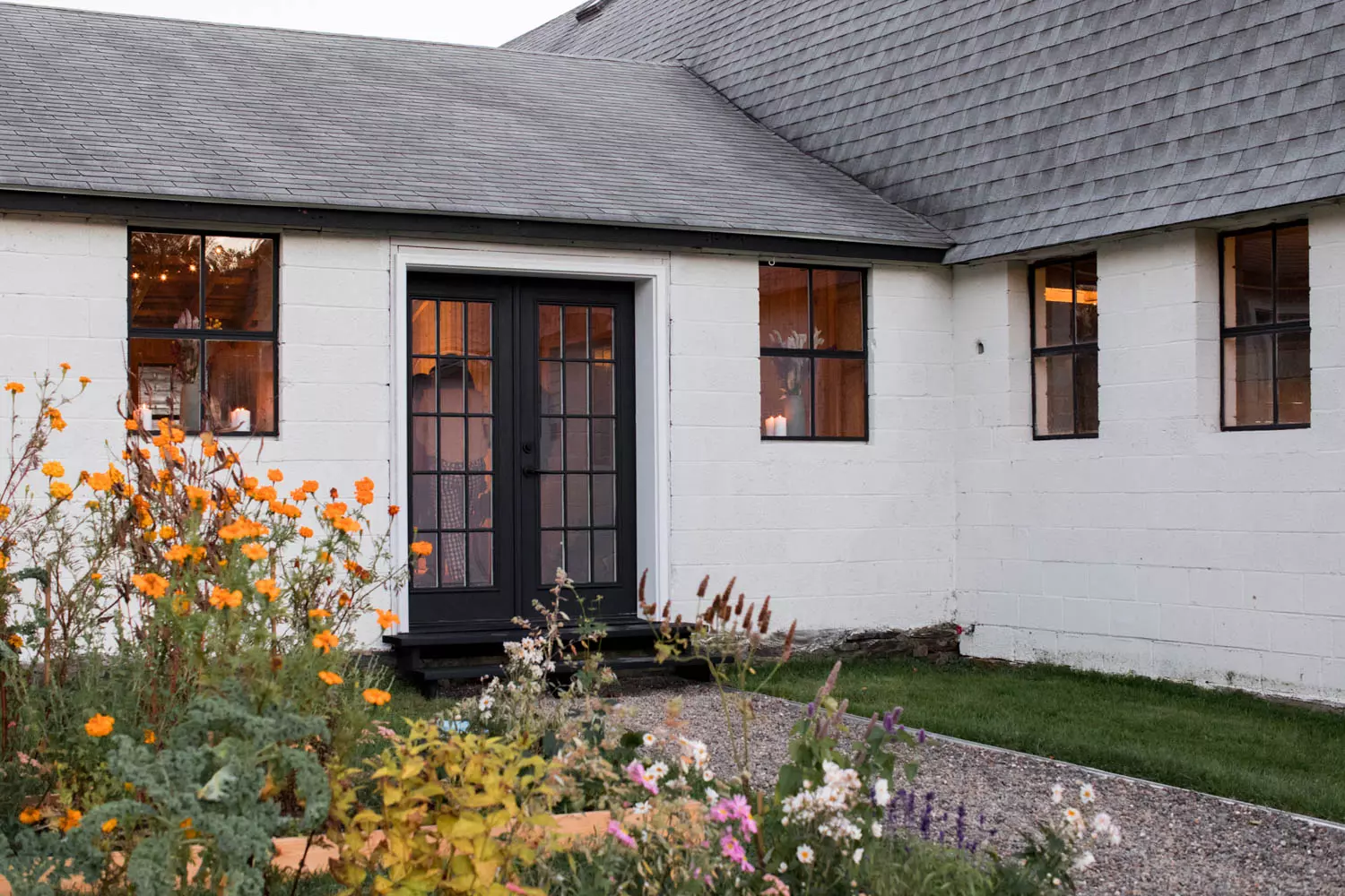 The exterior of a white farmhouse with wildflowers framing a path