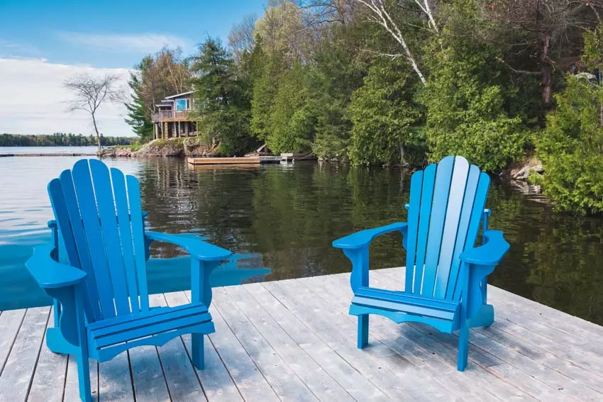 Two empty wood adirondack chairs sit on grass overlooking the mountains