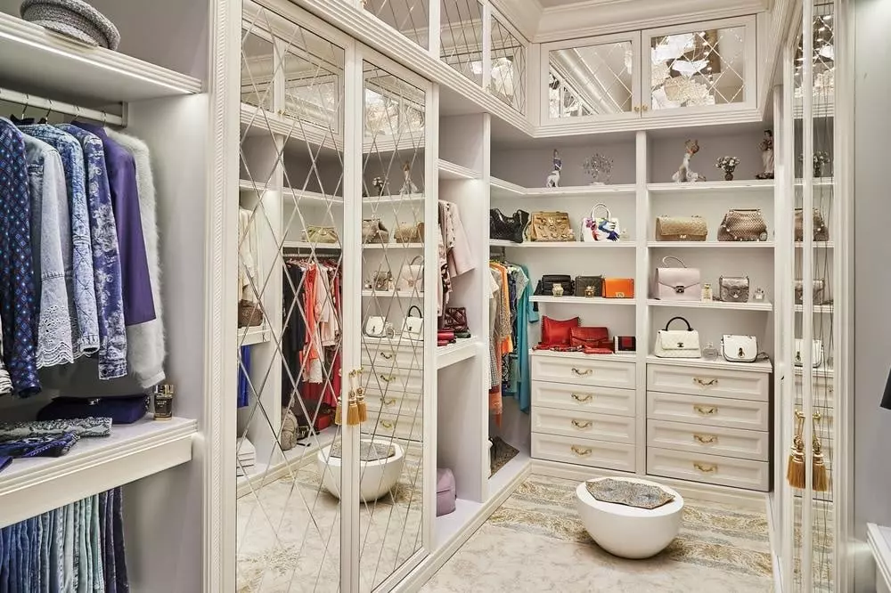 White luxury walk in closet full of clothes and has mirrors