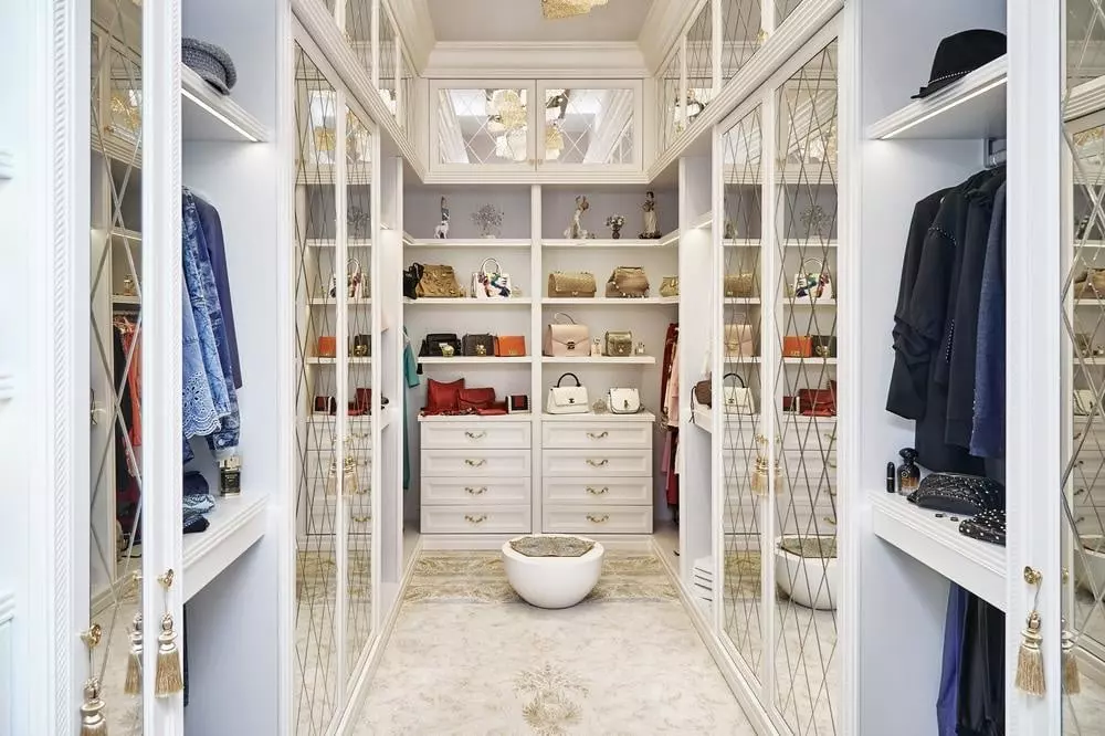 White luxury walk-in closet full of clothes and has mirrors on both sides