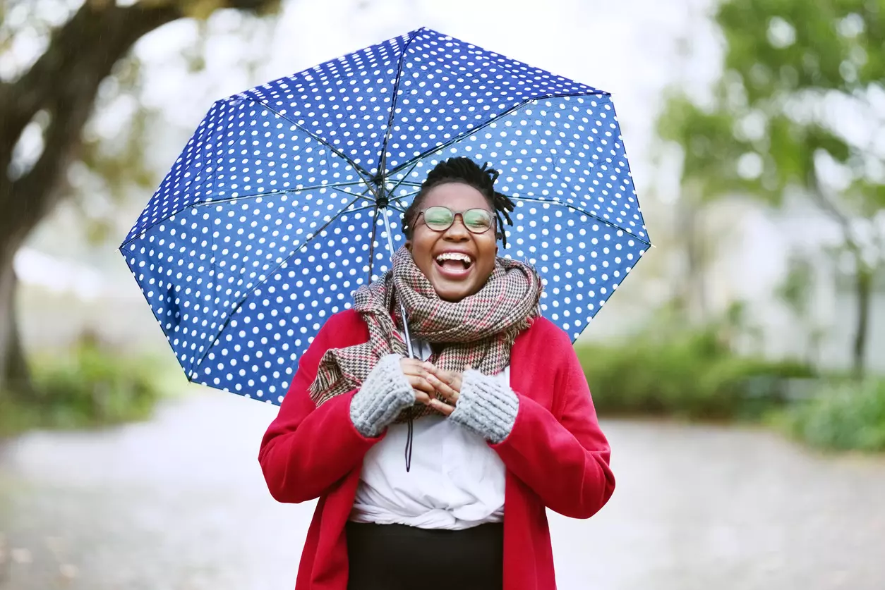 Shot of a cheerful young black woman under an umbrella in the rain