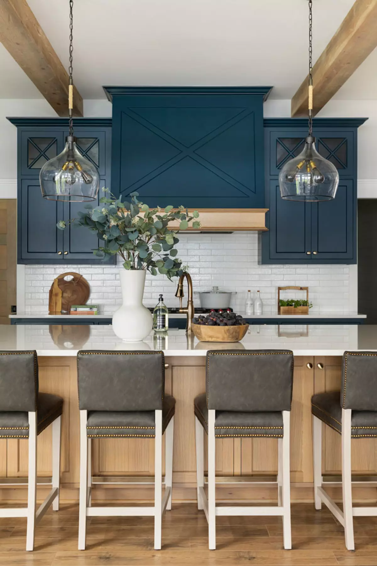 Navy blue kitchen cabinets with light wood island and brown leather stools