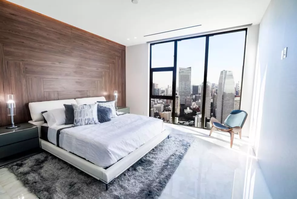 woman standing looking out of full-length window of luxury modern apartment or hotel room opening curtains in the morning enjoying sunlight and city skyscrapers