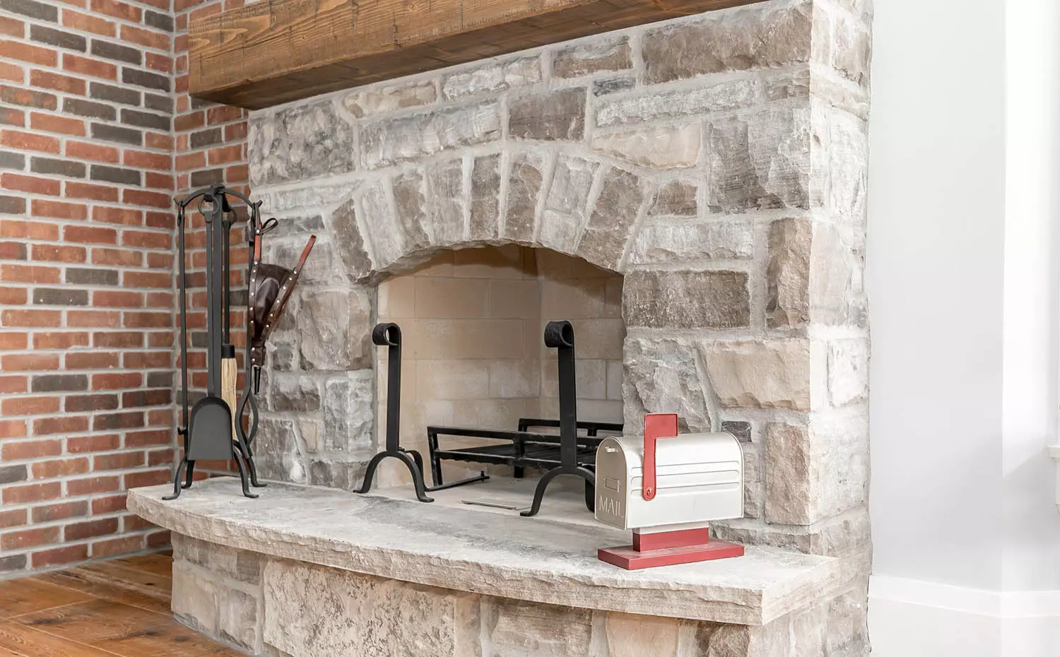 Red brick accent wall next to a stone wood-burning fireplace surround with tan brick insert. Thick timber floating mantle.