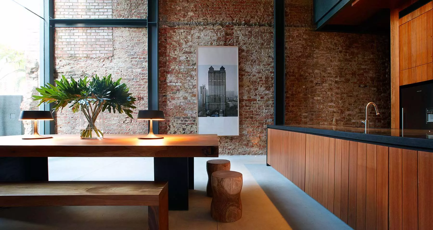 Modern apartment with a red brick feature wall, exposed black steel, wood cabinetry and furniture with concrete floors.