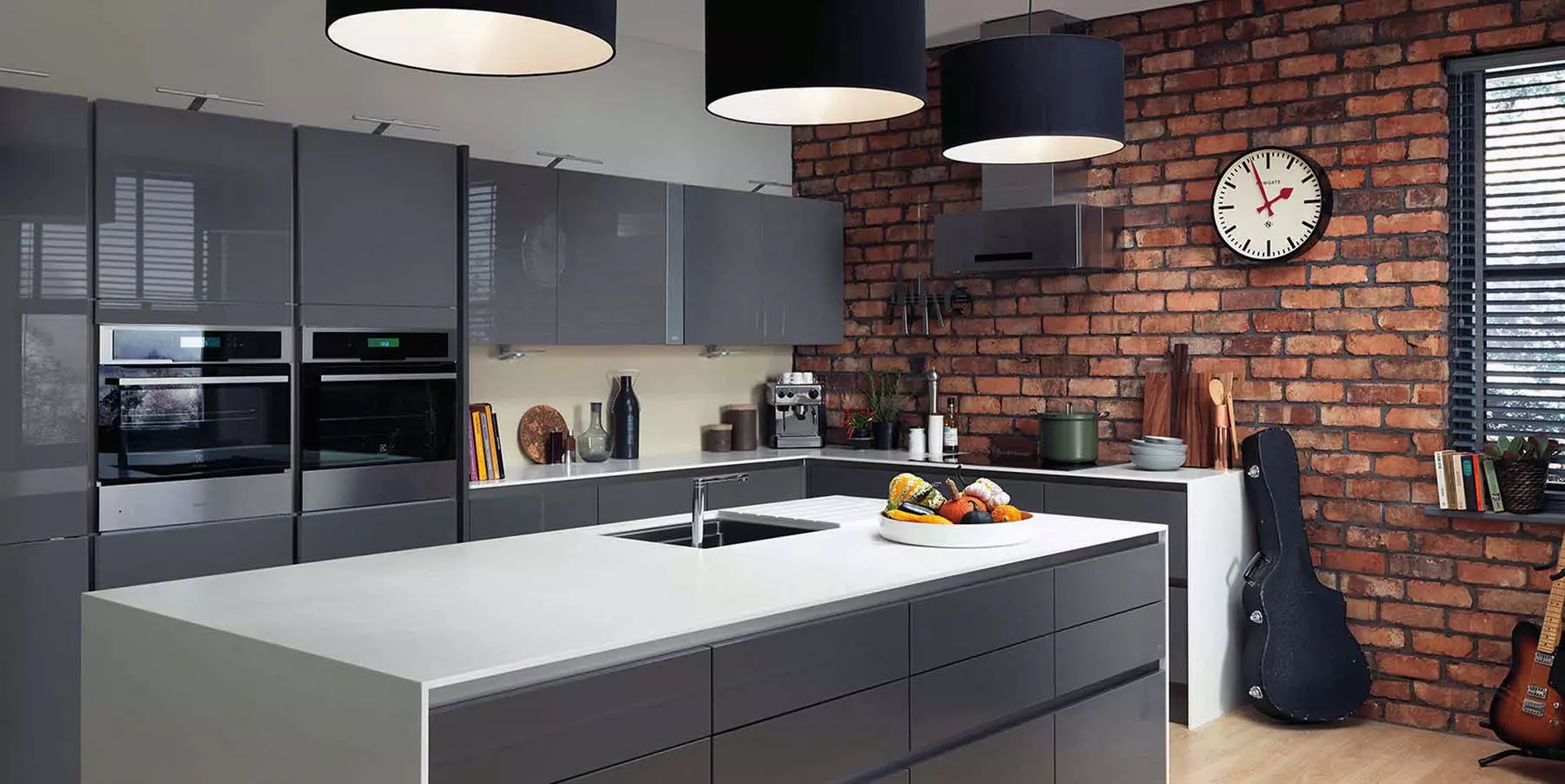 Modern kitchen featuring gray flat-faced cabinetry with no hardware, white countertops, and a red brick wall.