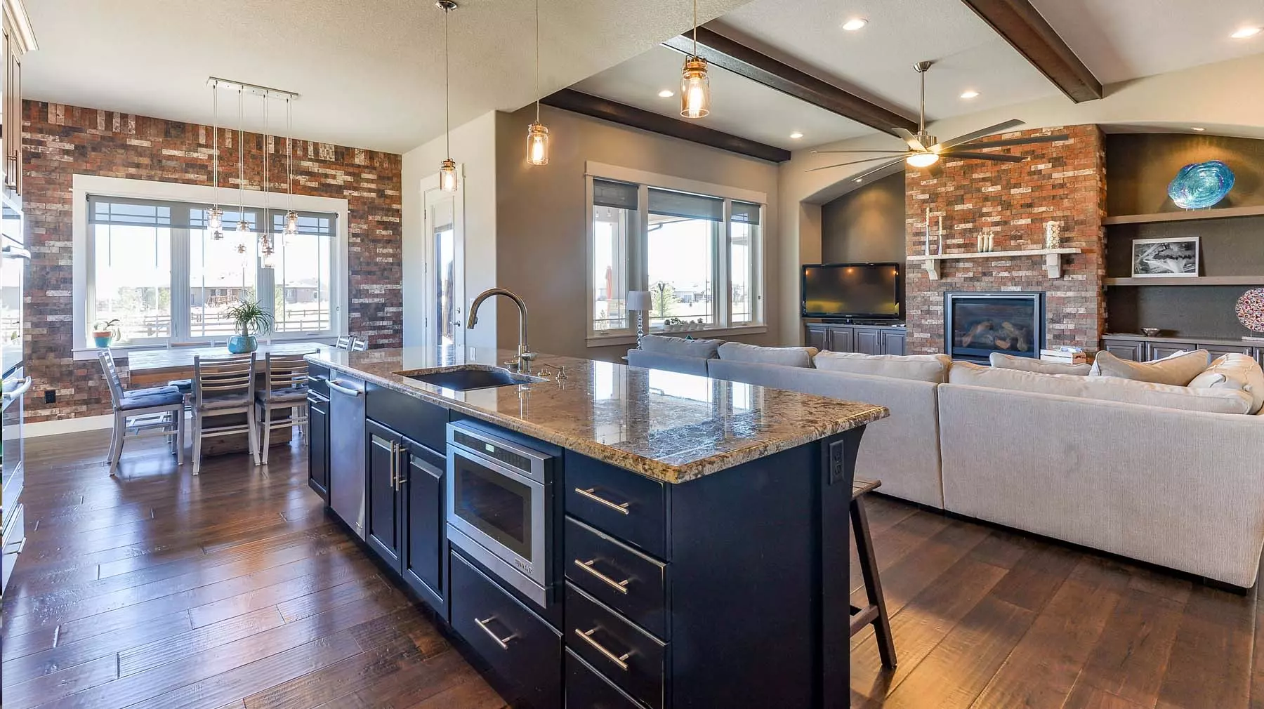 Open floor plan living room, kitchen, and dining area with matching red brick wall and fireplace.