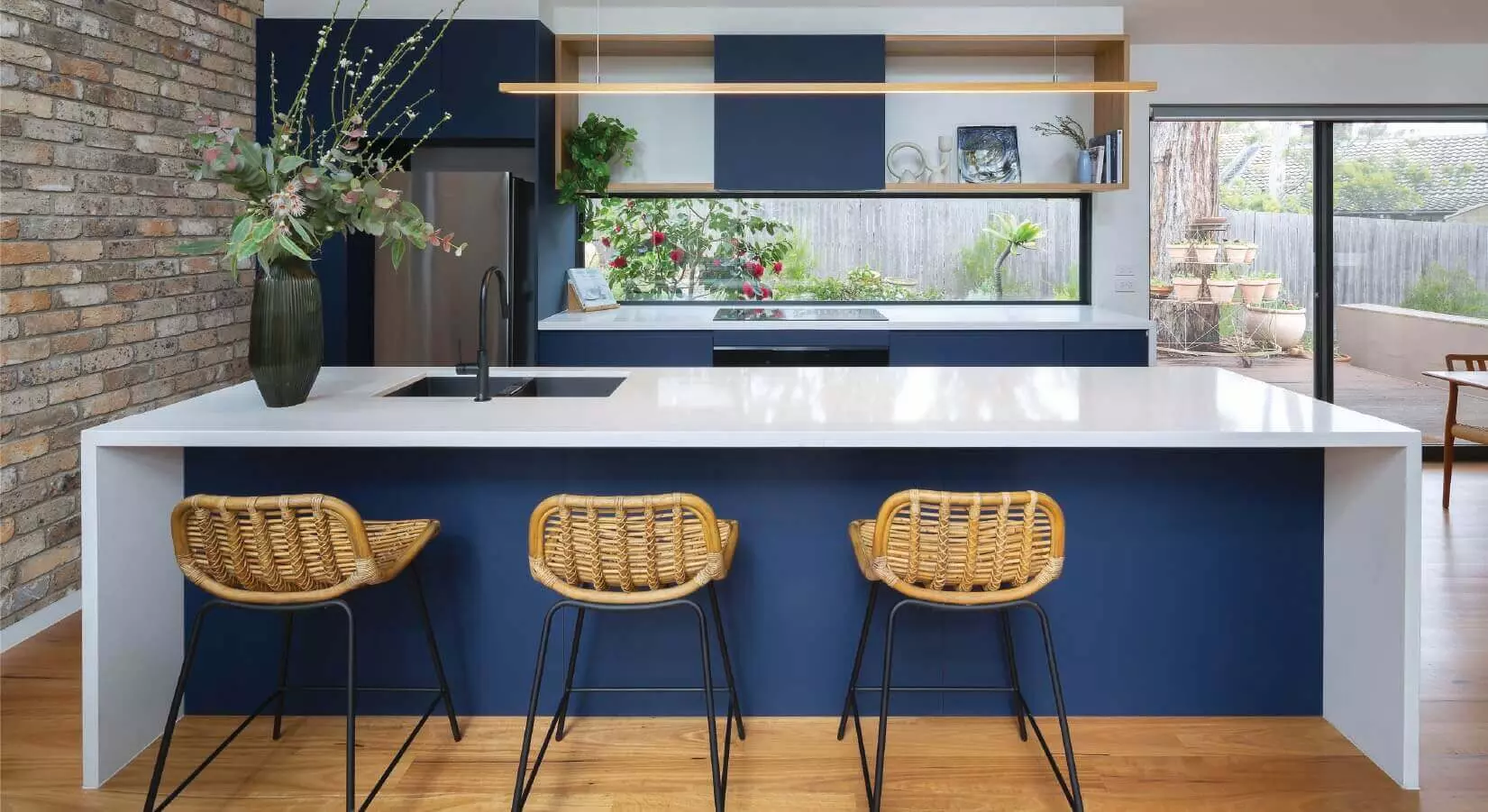 Kitchen with white waterfall island on top of blue countertop with rattan bar stools.